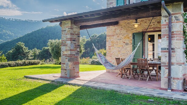 A stone building with a wooden porch, a hammock, and a table set for dining. - Villa / Independent home in Lucca with 3 bedrooms sleeps 6 (Lucca)