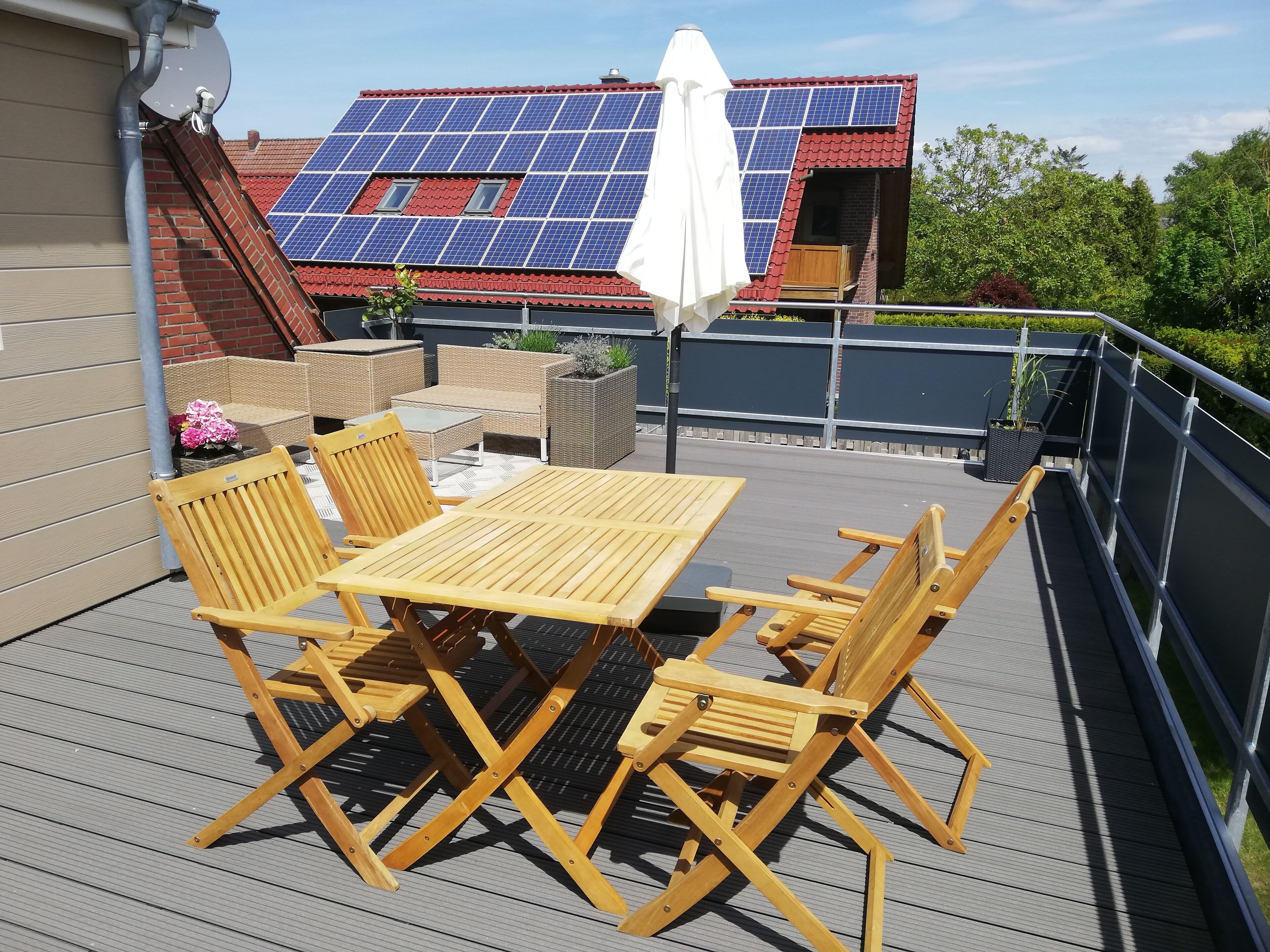 Eine Dachterrasse mit Tisch und Stühlen, einem weißen Sonnenschirm und Solaranlagen auf dem Dach.