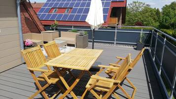 A rooftop terrace with a table and chairs, a white umbrella, and solar panels on the roof.