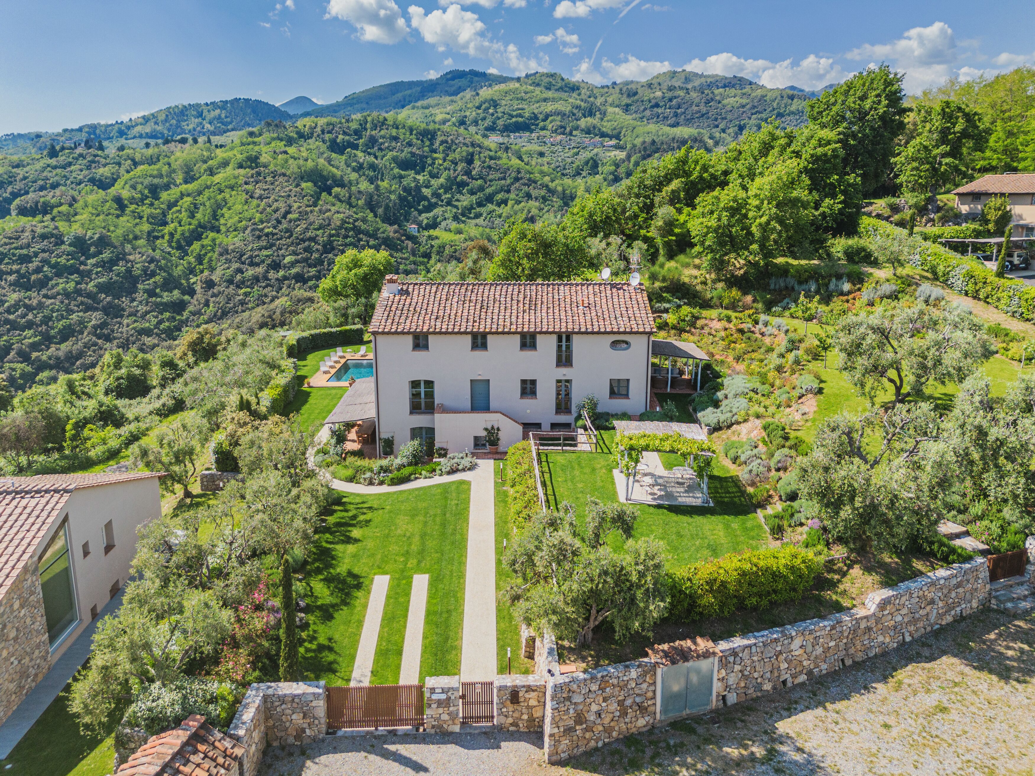 A two-story house with a tiled roof, surrounded by a well-maintained garden and a swimming pool.