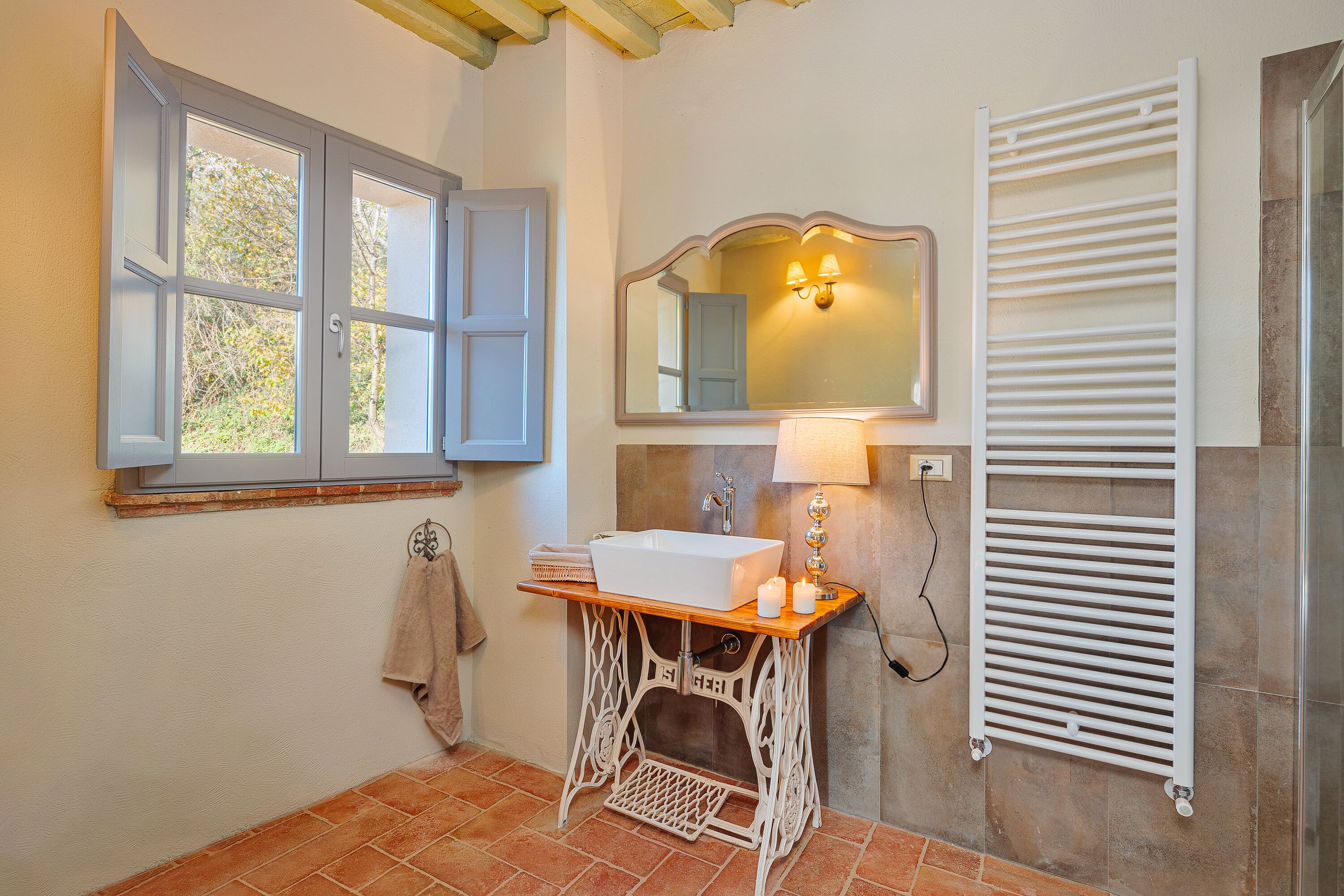 A bathroom with a white sink, a mirror, a towel rack, a window, and a radiator.