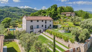 A white villa with a tiled roof, surrounded by lush greenery and a vineyard, set against a backdrop of rolling hills. - Villa / Independent home in Lucca with 5 bedrooms sleeps 10 (Lucca)