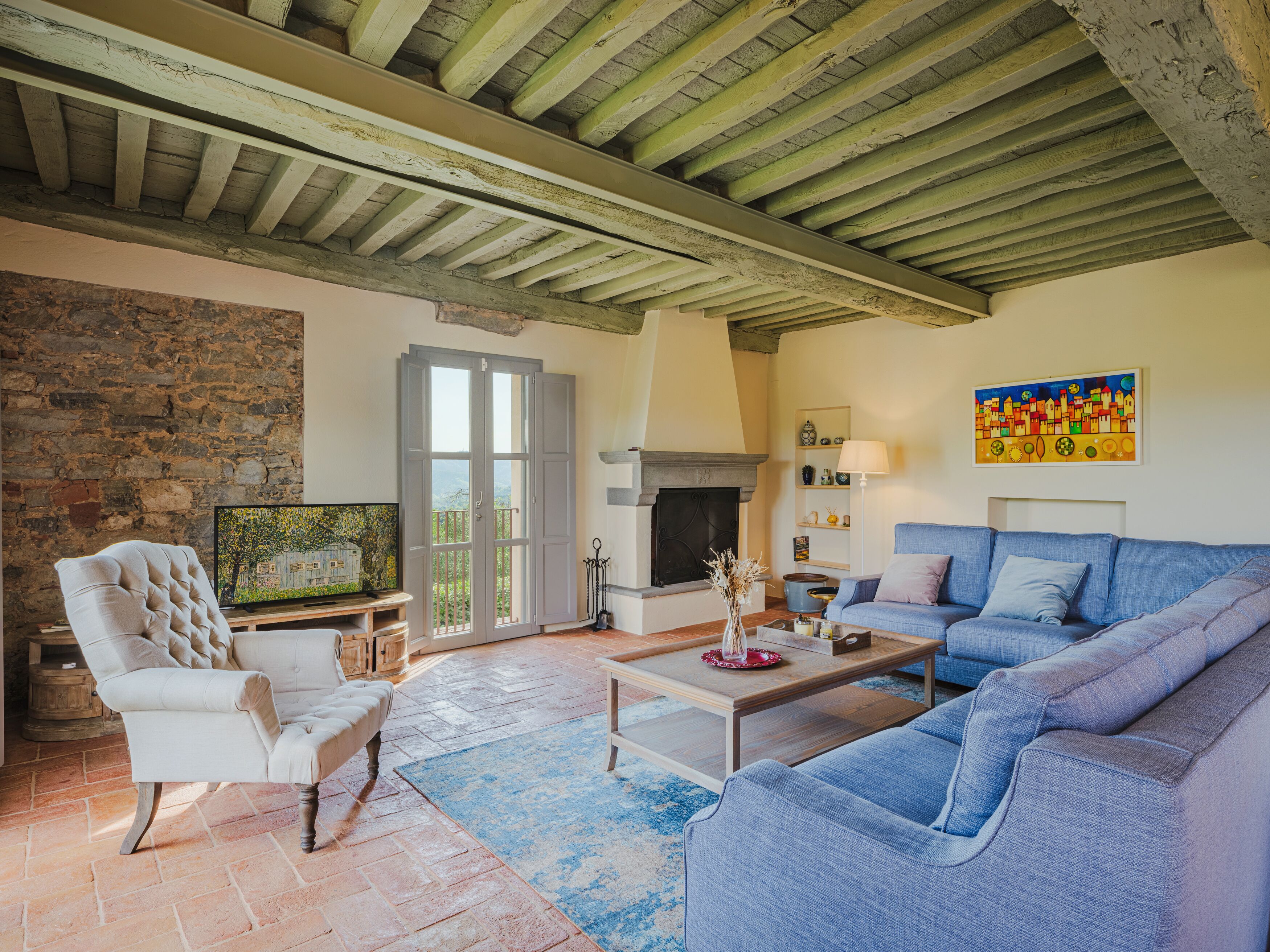 A living room with a stone wall, a fireplace, a sofa, a television, and a balcony door.