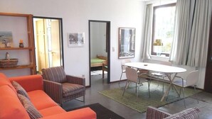 A modern living room with a sofa, striped armchairs, a dining table with chairs, and a large window with curtains. - Old school goting, classroom (Nieblum)
