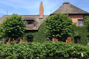 A traditional building with a thatched roof, ivy-covered walls, and a chimney. - Old school goting, classroom (Nieblum)