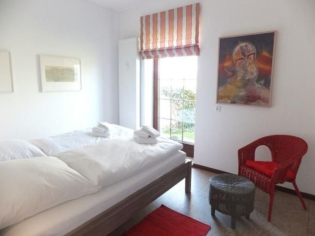 A bedroom with a bed, a window, a painting, and a red chair.