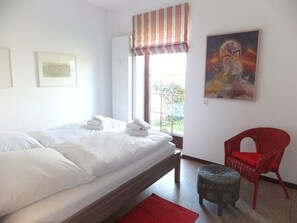 A bedroom with a bed, a window, a painting, and a red chair.