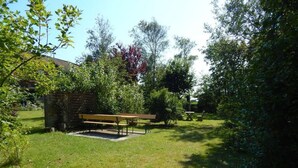 A grassy outdoor area with a wooden bench and a small brick structure, surrounded by trees and shrubs.
