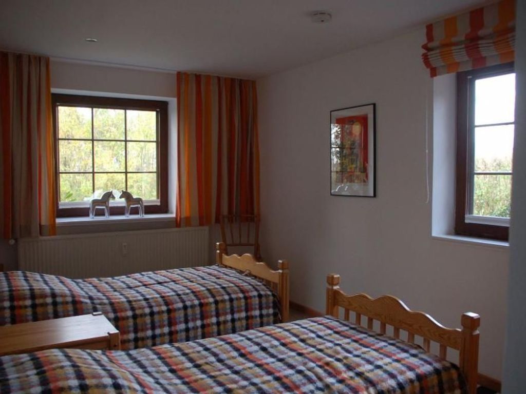 Ein Zimmer mit zwei Holzbett, einem kleinen Tisch und einem Fenster mit Vorhängen.