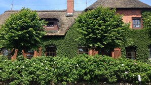 A traditional building with a thatched roof, ivy-covered walls, and a chimney.