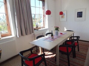 A dining area with a white table, red cushioned chairs, a patterned rug, and a window with curtains. - Old school Goting, southern class (Nieblum)