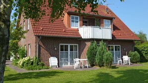 A two-story brick house with a red-tiled roof, a balcony, and a patio with outdoor furniture.