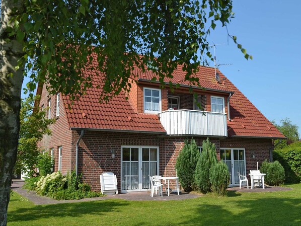 A two-story brick house with a red-tiled roof, a balcony, and a patio with outdoor furniture.