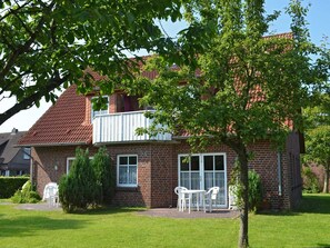 Une maison à deux étages, construite en briques, dotée d’un balcon, d’une pelouse devant et d’une petite terrasse avec du mobilier d’extérieur.