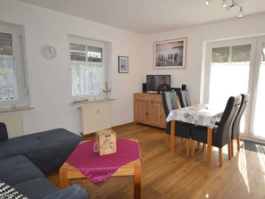 A living room with a sofa, a dining table with chairs, a wooden cabinet, a radiator, and a painting on the wall.