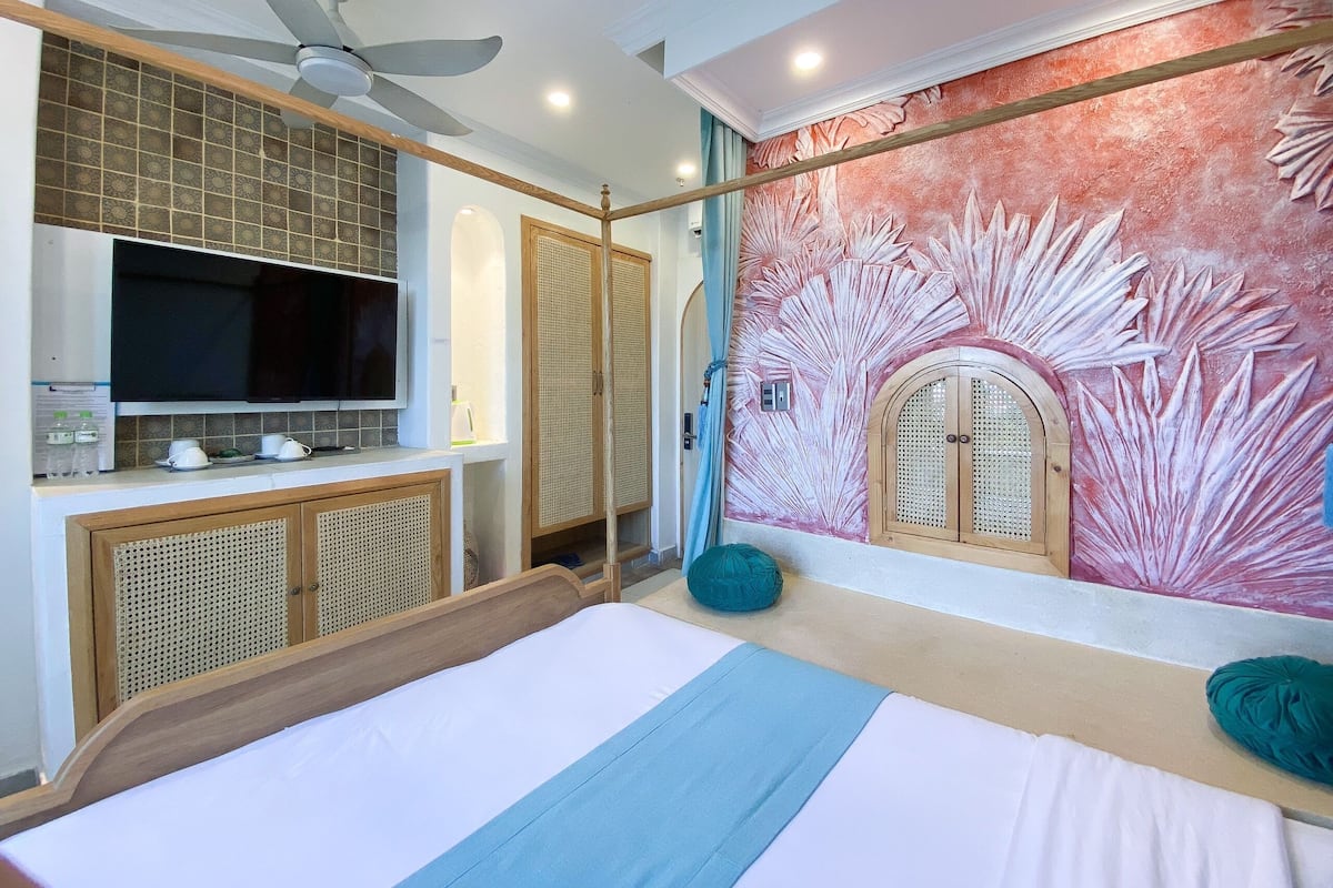 Een slaapkamer met een bed, een plafondventilator, een aan de muur bevestigde televisie en een decoratief muurschildering.