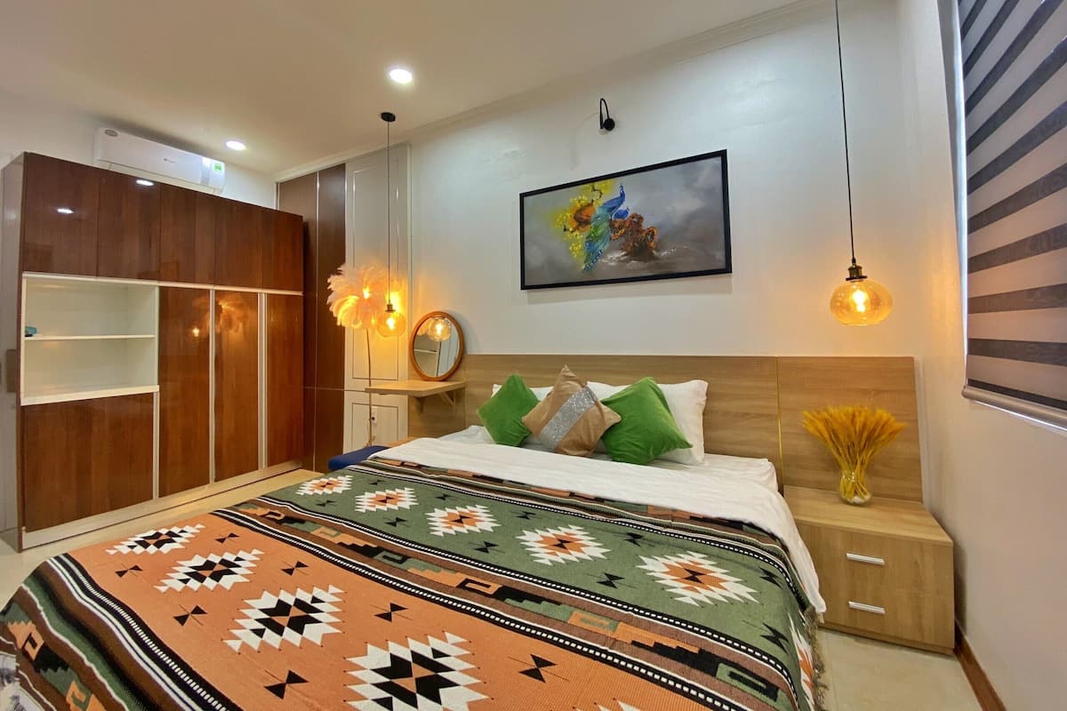 Een slaapkamer met een bed, een kledingkast, een nachtkastje, een spiegel en een schilderij aan de muur.