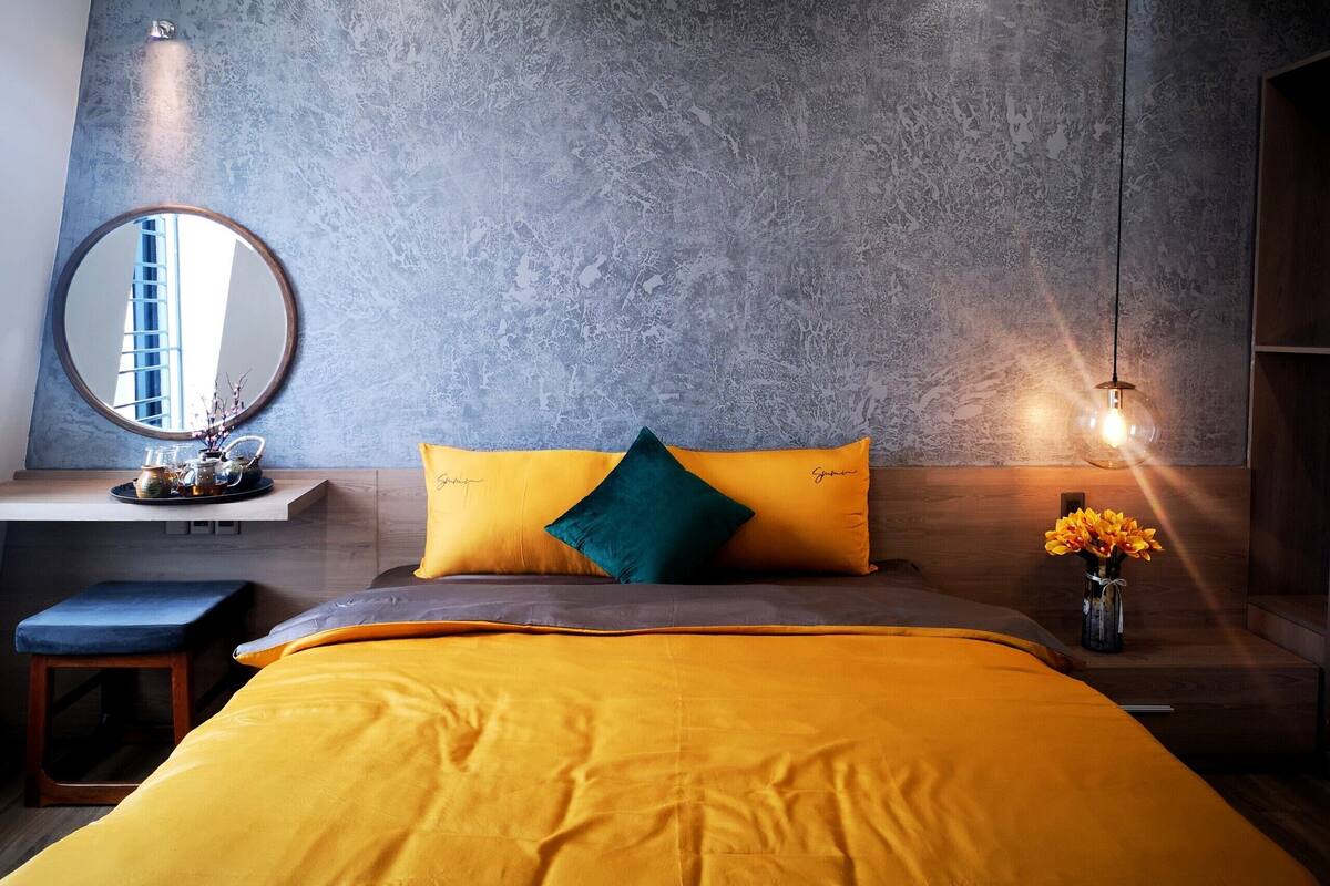 Een slaapkamer met een bed, nachtkastje, spiegel en een wandlamp.