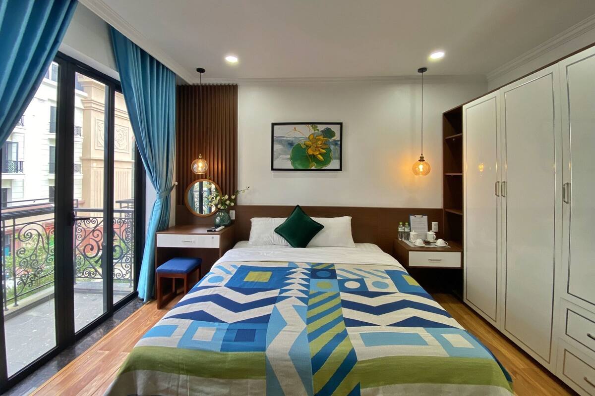 Een hotelkamer met een bed, een bureau, een stoel, een kledingkast en een balkon met uitzicht op gebouwen.