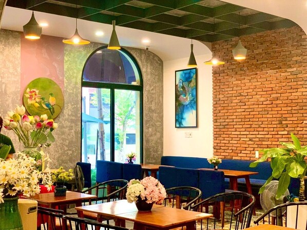 Interior de restaurante con mesas, sillas, lámparas colgantes, un ventanal grande y una pared de ladrillo.