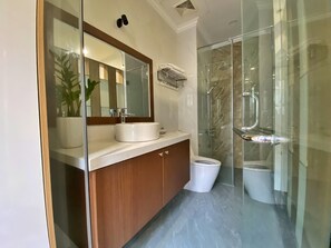 Un baño moderno con cabina de ducha de vidrio, un lavamanos blanco y un mueble de tocador de madera.