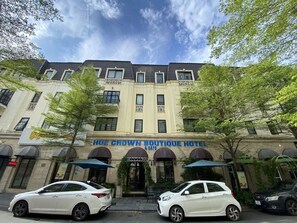 Un hotel con fachada clásica, dos coches estacionados al frente, y cielo despejado.