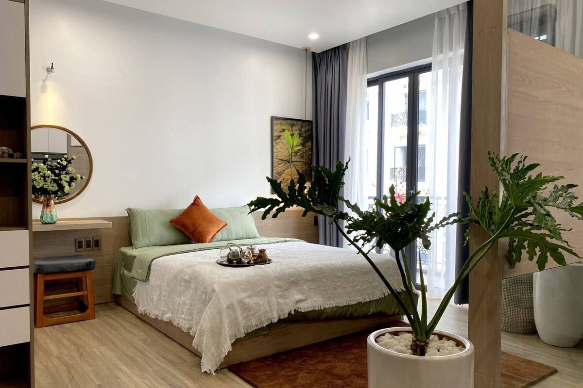 Een moderne slaapkamer met een bed, nachtkastje, spiegel en een potplant.