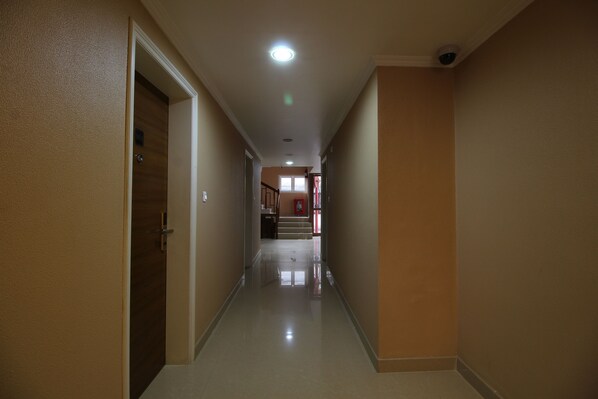 A hallway with a polished floor, beige walls, and a door on the left. - Srivar Hotels (Chavakkad)