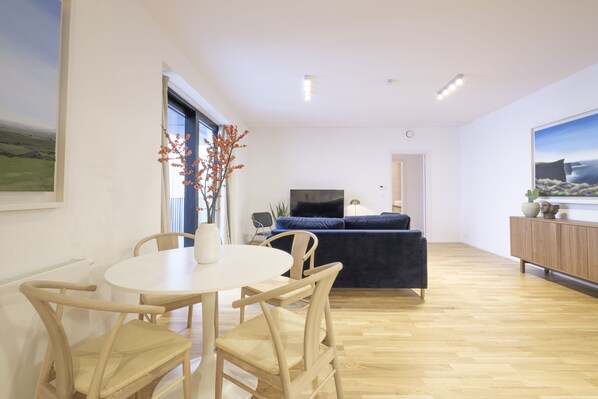 A modern living room with a dining area, featuring a round table, wooden chairs, a sofa, and a TV.