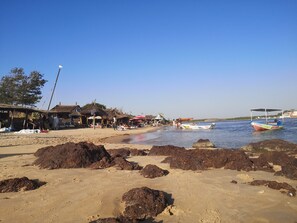 Una playa con cabañas de techo de paja, orilla arenosa y barcos en el agua.