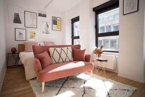 A modern bedroom with a pink sofa, a white fluffy rug, and a bed with a white headboard. - The Five Star (Brussels)
