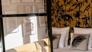 Una cama con ropa de cama blanca y un plaid negro, un cabecero de madera con diseño de bambú y cuadros enmarcados en la pared.