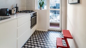 Una cocina compacta con armarios blancos, una estufa a gas y un banco rojo.