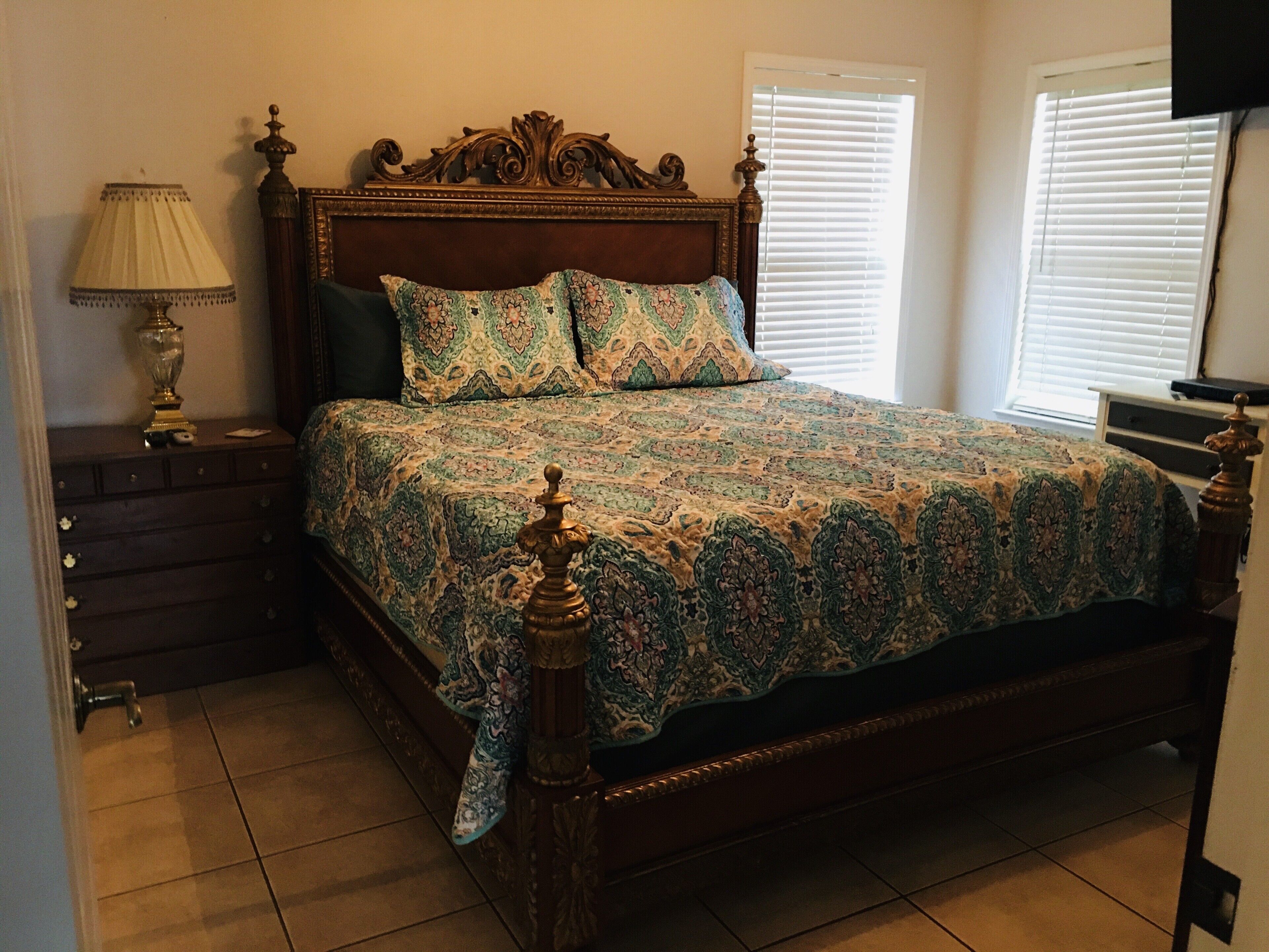 A bedroom with a wooden bed frame, patterned bedspread, and a nightstand with a lamp.