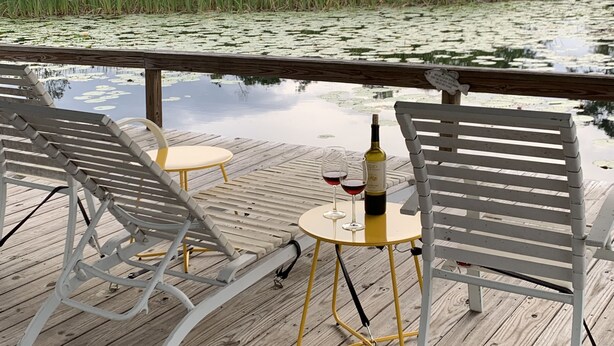 A wooden deck with two white lounge chairs and a small round table with a bottle and glasses. - The cottage of lake seminole (Donalsonville)