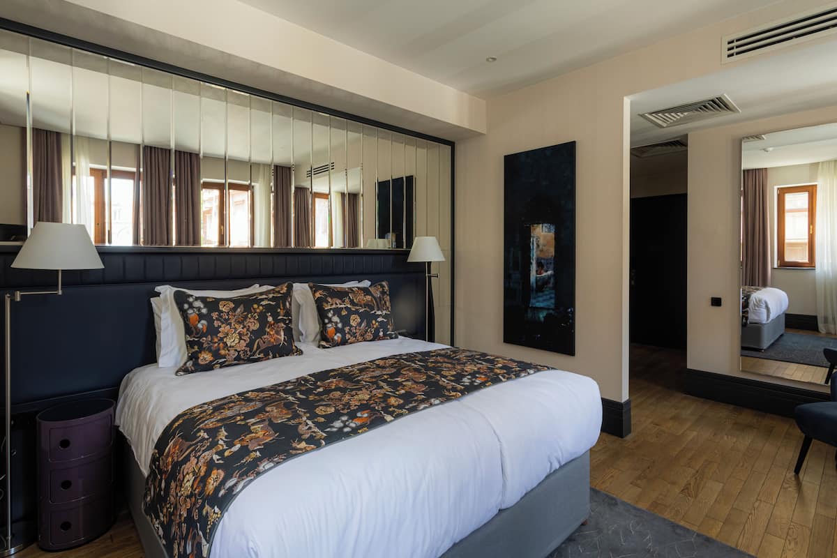 Een hotelkamer met een groot bed, een spiegel boven het bed, een nachtkastje, een lamp en een schilderij aan de muur.