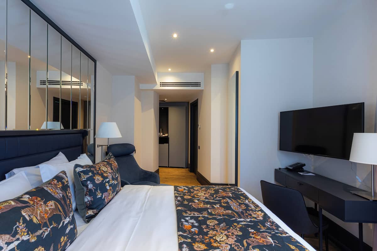 Een moderne hotelkamer met een groot bed, een bureau met een flatscreen televisie, een spiegel en uitzicht op de gang.