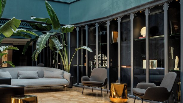 A spacious atrium with a modern design, featuring a seating area with sofas and armchairs, a decorative chandelier, and large windows offering views of the interior. - Boutique Hotel Puris Moedani (Tbilisi)