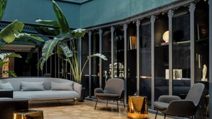 Un amplio atrio de diseño moderno, con zona de estar que incluye sofás y sillones, una lámpara decorativa y grandes ventanales con vistas al interior.