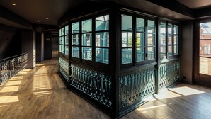 A corridor with wooden flooring, a black decorative railing, and large windows with a view of a building outside. - Boutique Hotel Puris Moedani (Tbilisi)