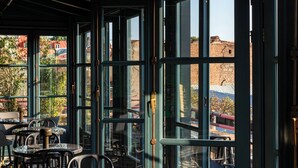 An indoor seating area with tables and chairs, large windows, and a view of buildings outside. - Boutique Hotel Puris Moedani (Tbilisi)