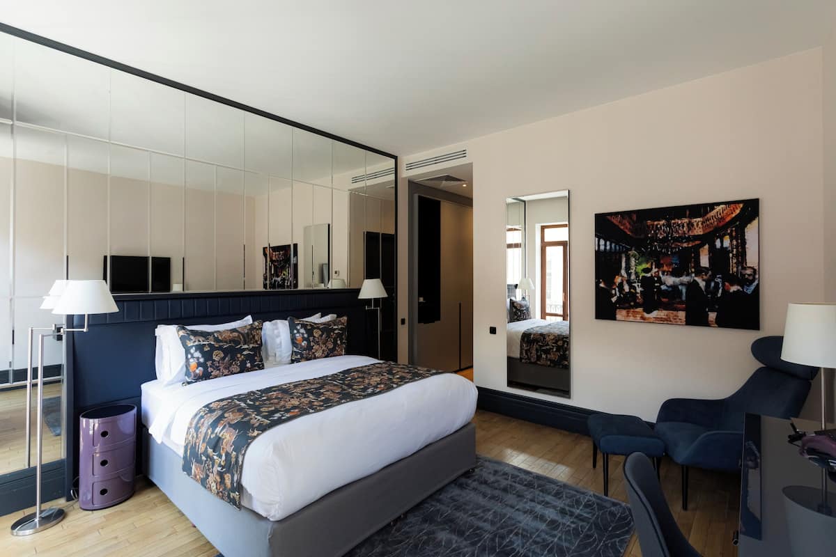 Een moderne hotelkamer met een groot bed, een zithoek, een schilderij en een grote spiegel.