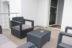 A balcony with wicker furniture, including a chair and ottoman, and a glass door leading to an interior space. - Chillinghouse 9 (Siegburg)