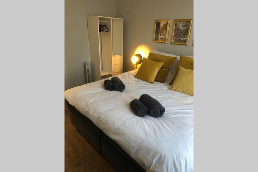 A neatly made bed with white linens and two rolled towels, a bedside lamp, and a wardrobe with a hanging rack.