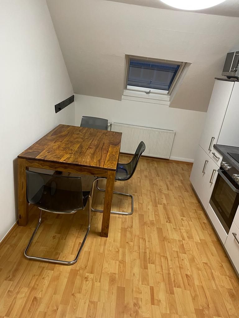Una cocina pequeña y funcional con una mesa y sillas de madera, una ventana y un horno empotrado.