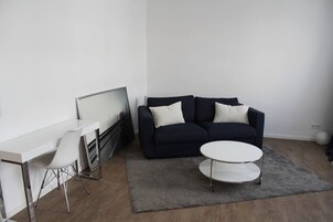 Uma sala de estar moderna com um sofá azul escuro, uma mesa de centro branca e uma escrivaninha branca com uma televisão de tela plana.