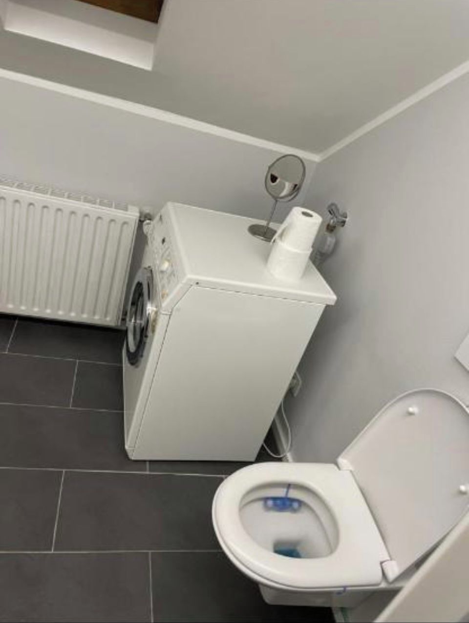A compact bathroom with a toilet, a washing machine, and a radiator.