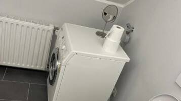 A compact bathroom with a toilet, a washing machine, and a radiator.