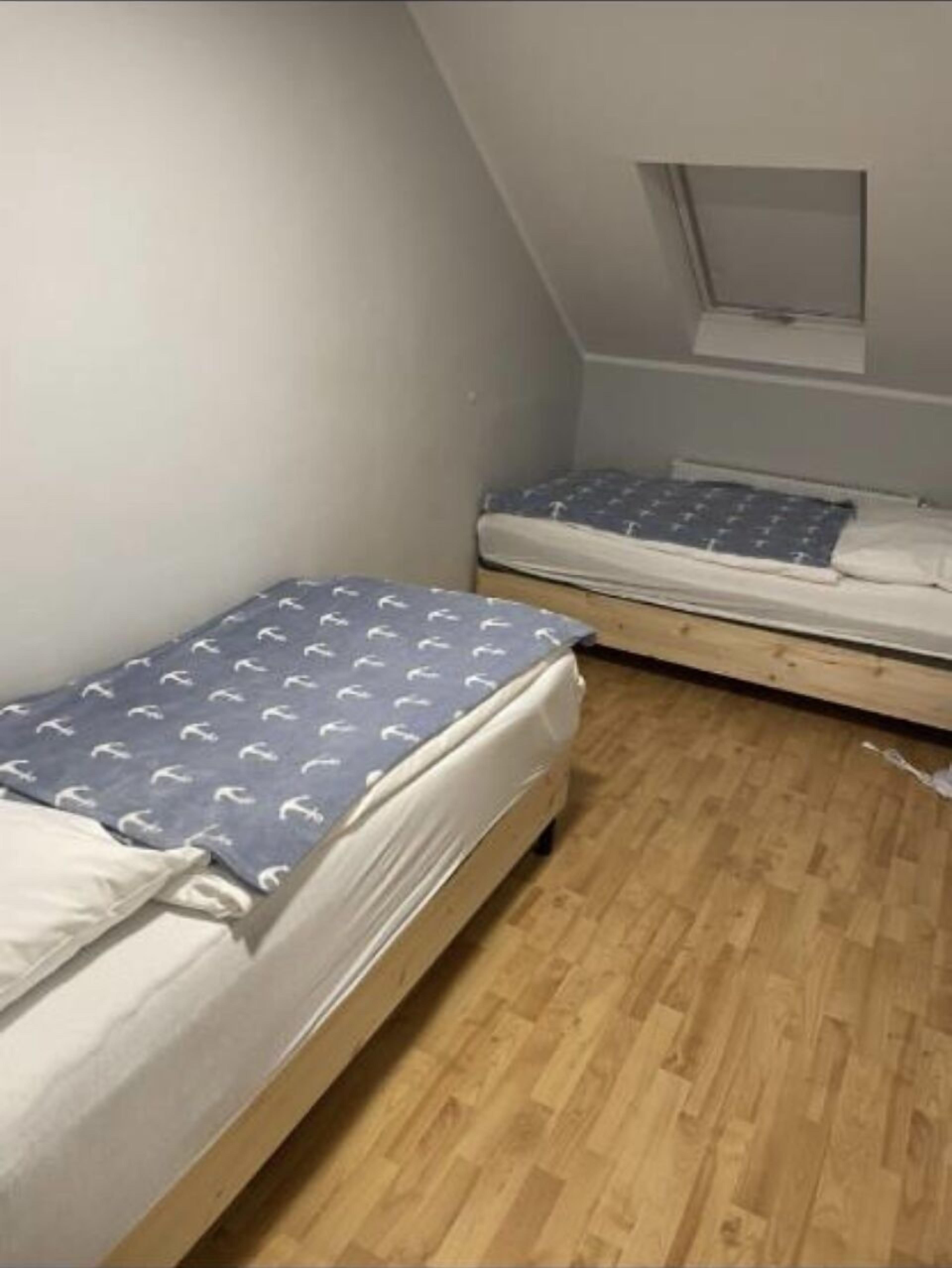 A small, dimly lit room with two single beds, wooden flooring, and a sloped ceiling with a skylight.