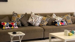 A living room with a brown sofa, patterned cushions, a small white side table, and a white coffee table. - Muhanna Chalets (Al Khiran)